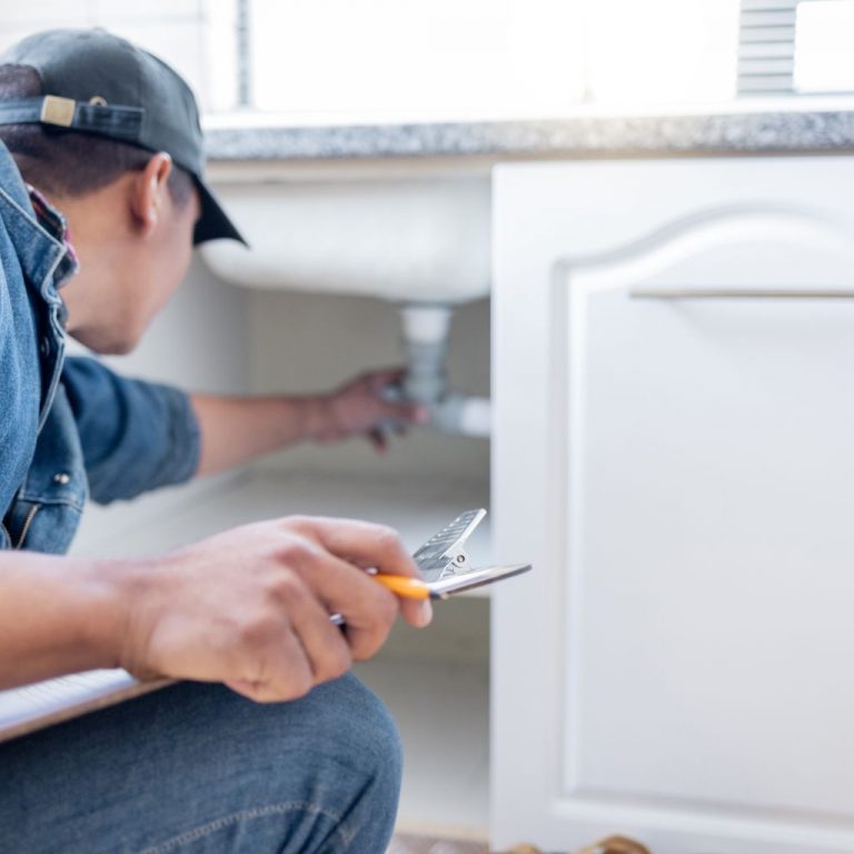 Home inspector examining plumbing under a sink for leaks and proper drainage